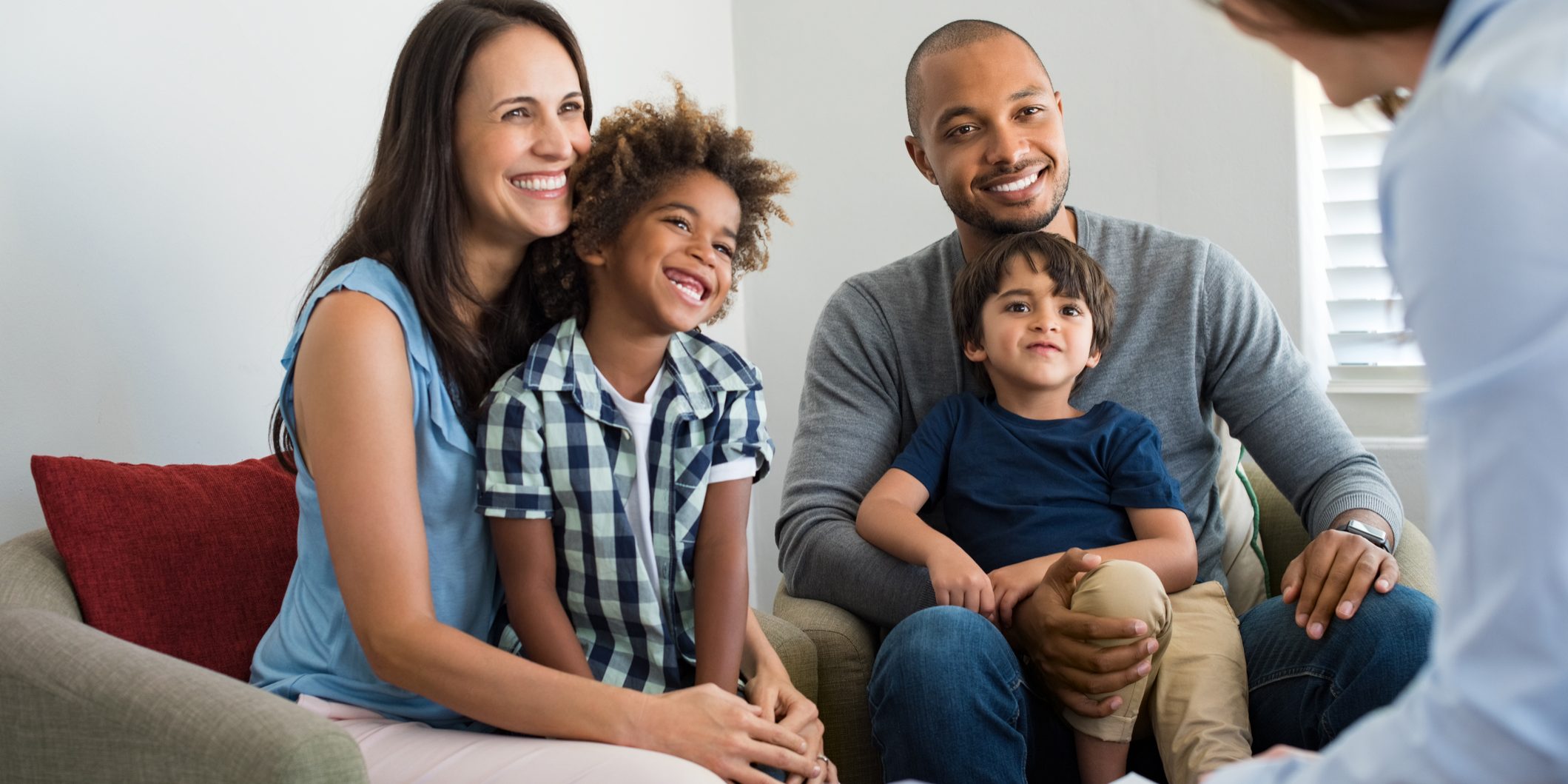 Happy young family sitting on couch and talking with family counselor. Smiling parents with adopted children discussing with counselor. Multiethnic family meeting a financial agent.